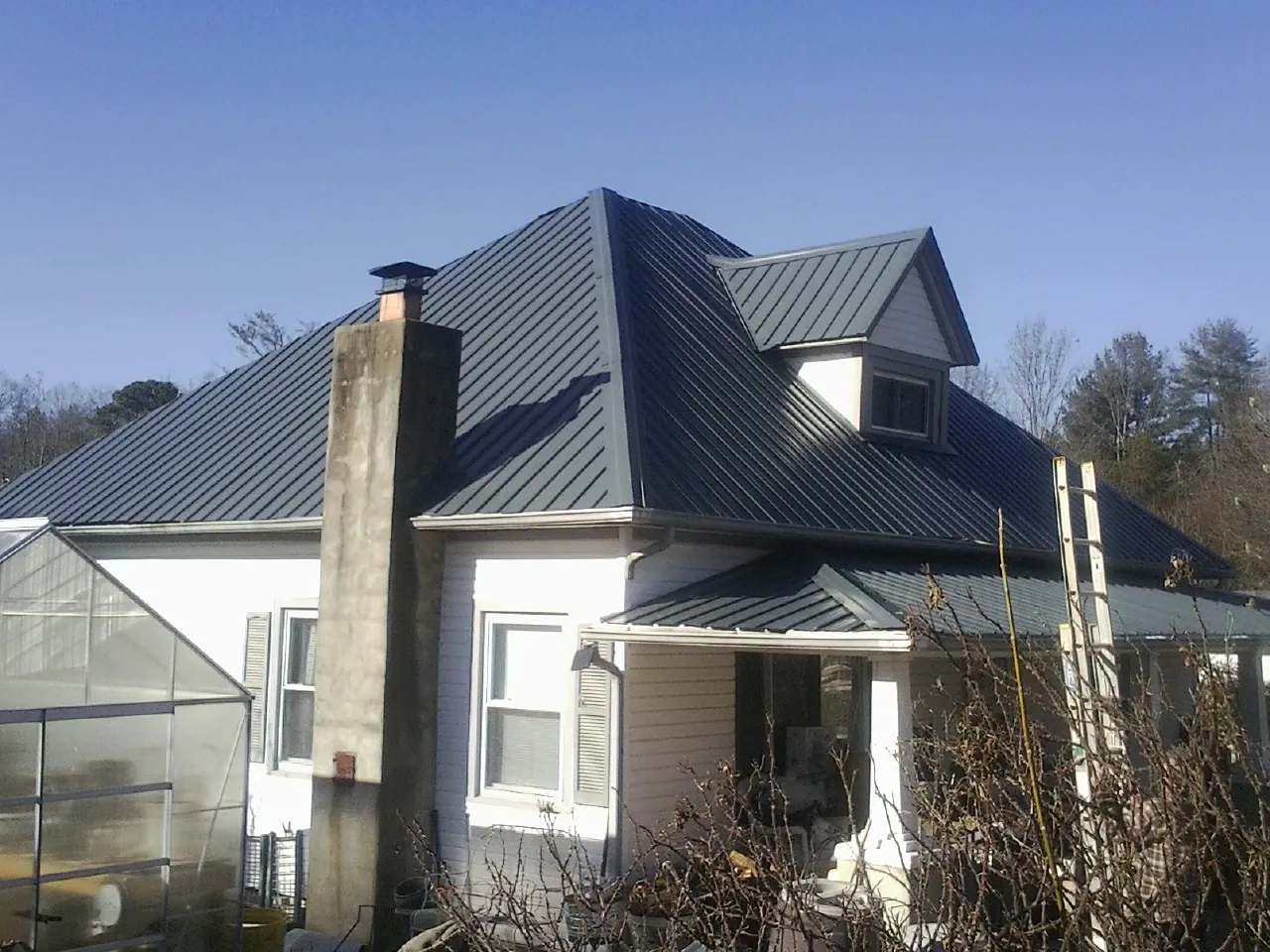 Dark blue standing seam metal roof on a white farmhouse with dormer — Slate & Tile Roof Repair by Roofing Brothers in Port Haywood