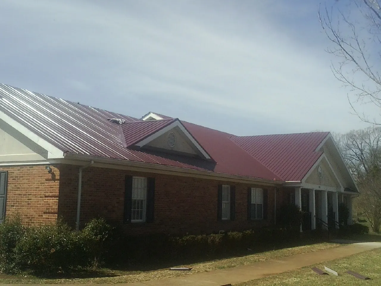 Red metal roof with gabled entries on a long brick building, from a Hail Damage Roof Repair job in Port Haywood