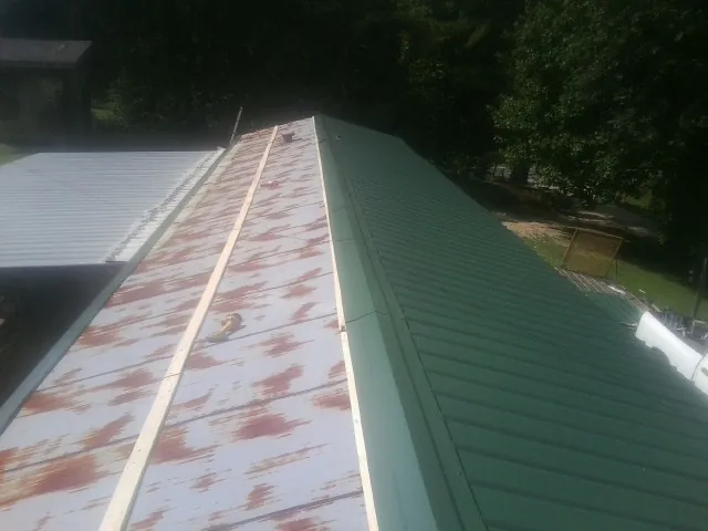 Old rusted panels beside newly installed green metal roofing — Wind Damage Roof Repair by Roofing Brothers in Port Haywood