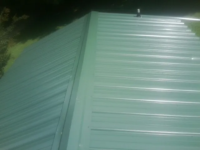 New green metal panels meeting at the ridge of a roof — Flat Roof Repair work by our crew in Port Haywood