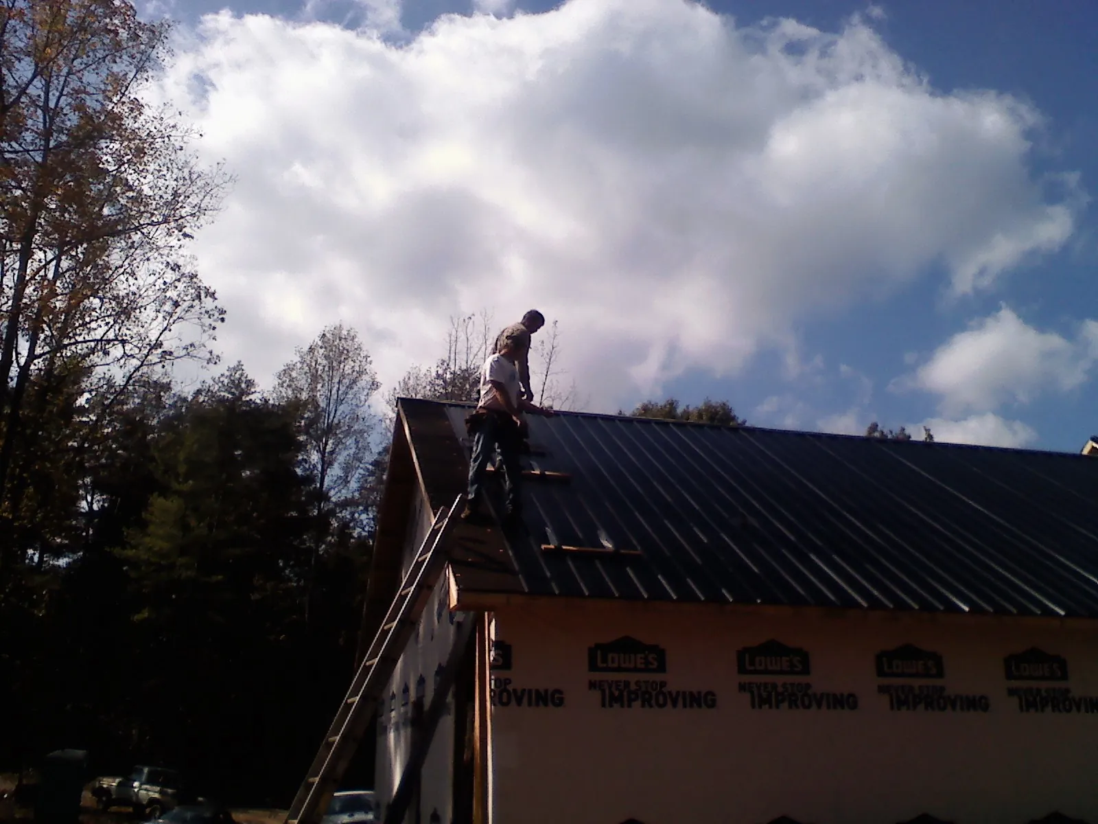 Roofer fastening dark metal panels high against a cloudy sky, from a Roof Inspection job in Port Haywood