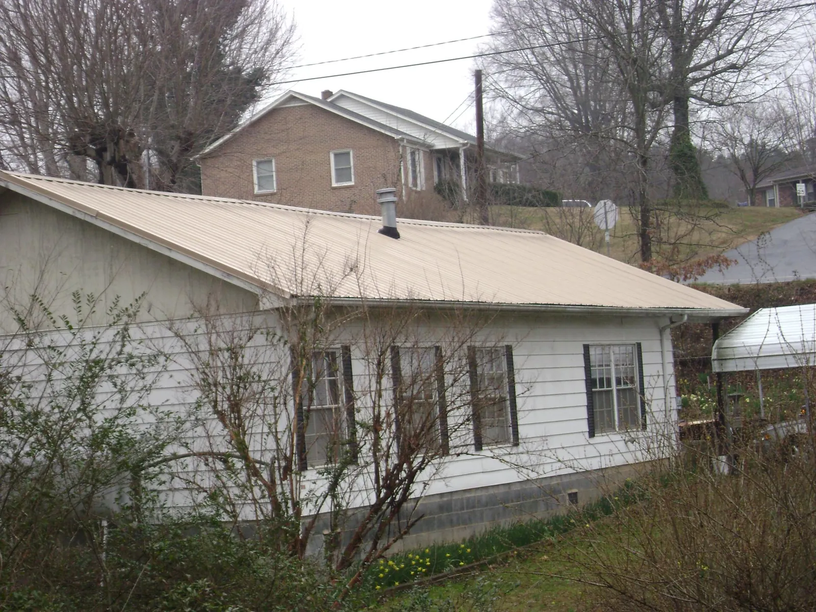 Tan metal roof on a white sided house set into a hillside — Commercial Roofing by Roofing Brothers in Port Haywood