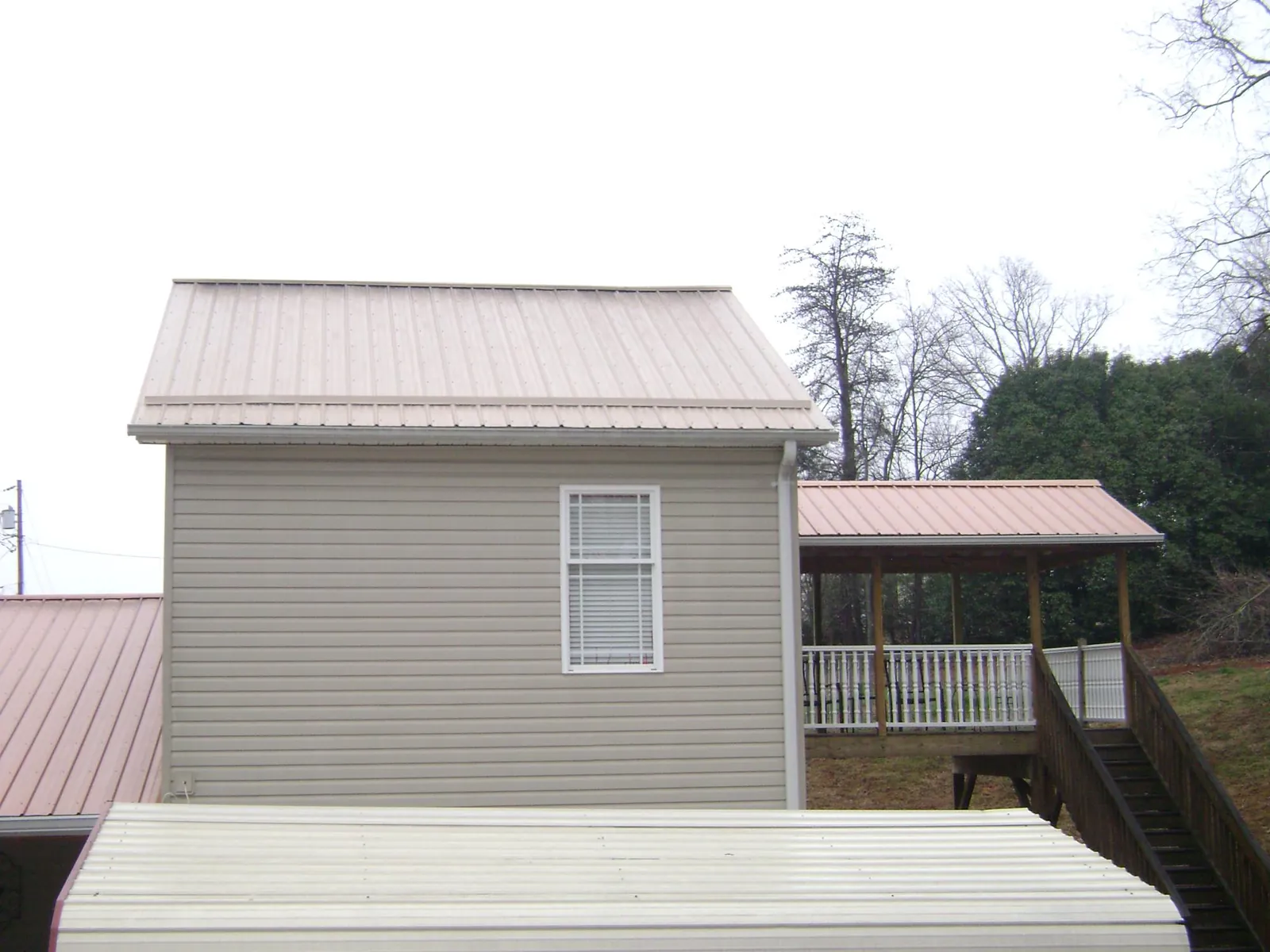 Tan metal roofs on a two story addition and attached porch, from a Roof Replacement job in Port Haywood